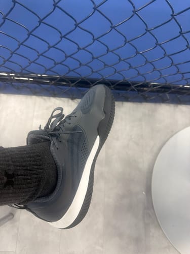 Customer's dark grey CUURT Muuv court shoe with white sole worn with a black sock against a chain-link fence.