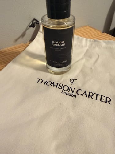 Customer's Rouge Avenue Eau de Parfum bottle standing upright on a branded Thomson Carter cloth bag.