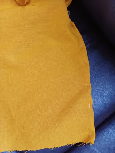 Customer's mustard yellow linen look polyester fabric pinned along the edge for a sewing project.