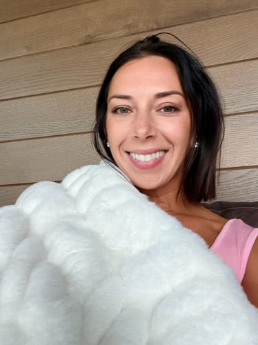 Reviewer smiling, wrapped in a plush cream Hugs Cream blanket with a textured fabric finish.
