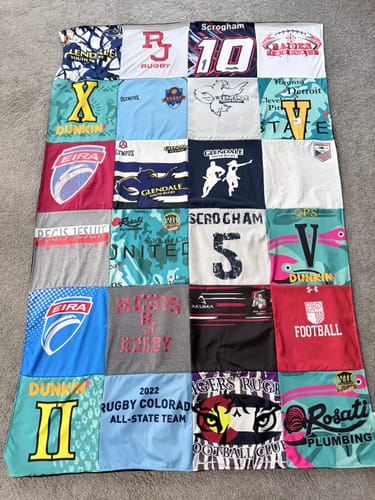 Customer's Project Repat T-Shirt Quilt featuring a colorful collage of rugby tour and team shirts on a carpeted floor.