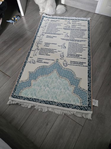 Customer's Step-by-Step Phonetic Salah Padded Prayer Mat spread on a gray floor with white decorative tassels.