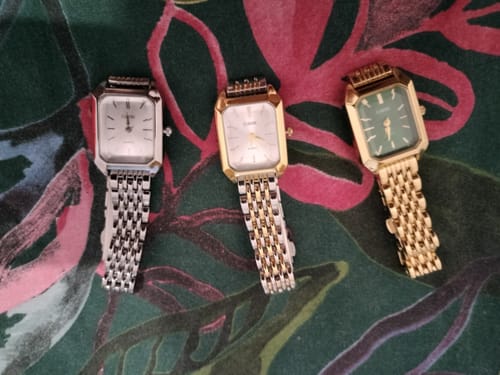 Customer's three Claire De Mains watches in silver, two-tone, and gold metal finishes resting on a floral background.