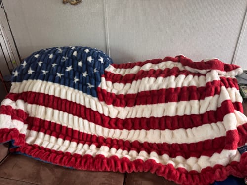 Customer's soft Hugs Flag Blanket with red, white, and blue pattern draped across a brown sofa.