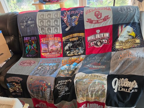 Customer's Project Repat T-Shirt Quilt draped over a leather sofa, showing various colorful t-shirt graphics.