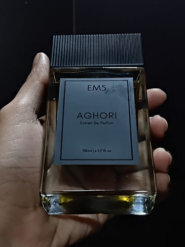 Reviewer's hand holding a glass bottle of Aghori Extrait De Parfum against a dark background.