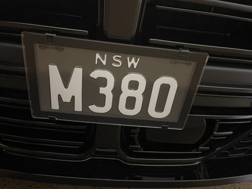 Customer's BMW M3/M4 OEM Plinth Delete Kit installed, securely mounting a black number plate to the front grille.