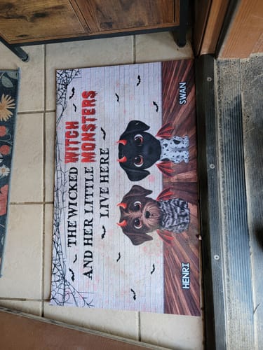 Customer's Halloween personalized doormat featuring two cute puppy illustrations, spiderwebs, and names on a floor.