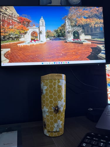 Customer's yellow To-Go Buddy tumbler with honeycombs and flowers sitting on a desk in front of a computer screen