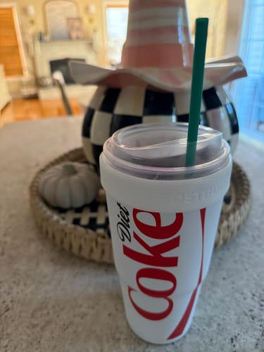 Customer's white Diet Coke To-Go Buddy tumbler with a green straw, resting on a kitchen tray with decorative items.