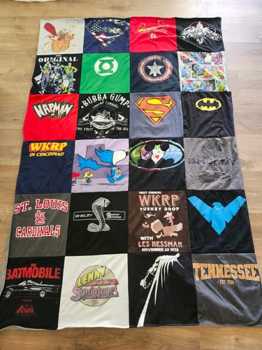 Customer's Project Repat T-Shirt Quilt featuring various graphic logos on a wood floor.