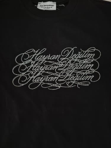 Müşterinin siyah, parlak taş baskılı Hayran Değilim yazılı Radikal Merch tişörtünün yakın çekimi.