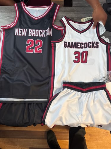 Customer's custom black and white basketball jerseys with team names and numbers displayed on a wooden surface.
