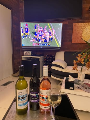Customer's three Little Ripples wine bottles and a filled glass on a table in front of a television showing football.