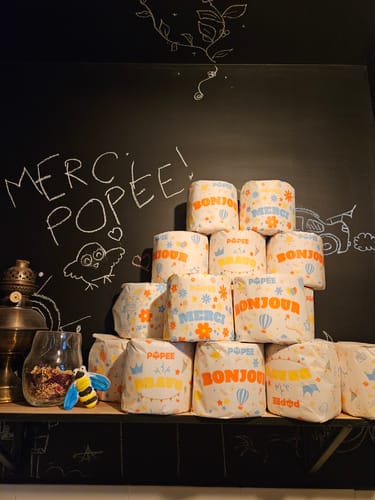 Customer's Papier Toilette Édition DÉCO en rouleaux empilés devant un tableau noir écrit à la craie.