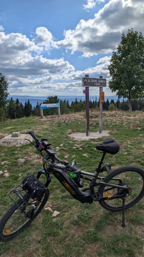 Customer's Lankeleisi MG600 Pro e-mountain bike parked on a mountain trail near a scenic signpost.