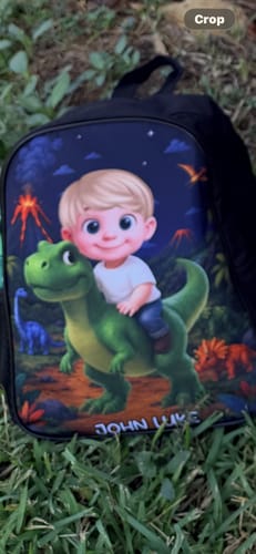 Customer's personalized dinosaur backpack with a custom cartoon child graphic and name label, resting on grass.