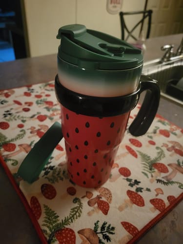 Customer's To-Go Buddy handle attached to a red watermelon-patterned cup with a green lid on a mushroom-print mat.