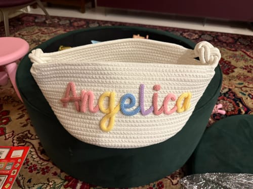Customer's white knitted basket with the personalized name Angelica in multicolored yarn letters.