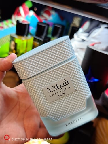 Reviewer's hand holding the light blue Khadlaj Shiyaaka Sky perfume bottle with a textured, studded cap.