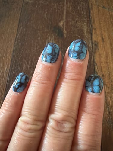 Customer's hand with Blue Winged Magic UV Gel Nail Wraps showing blue butterfly patterns on black base after one week.