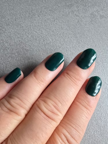 Reviewer's hand showing applied UV Gel Nail Wraps in a deep, rich green color on clean fingernails.