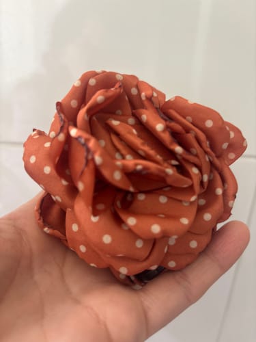 Customer's Pinche Flor Puntos, una flor de tela color terracota con puntos blancos sostenida en una mano