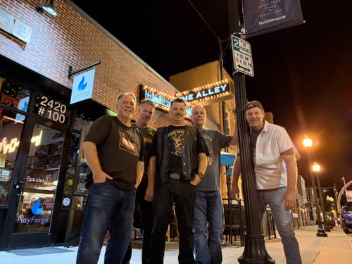 Customer's band members wearing dark Rocks & Roll Whiskey T-Shirts while standing outside a venue at night.