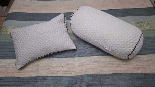Customer's Forro de Lumbar blanco, incluyendo una almohada rectangular y una cilíndrica sobre una cama a rayas.