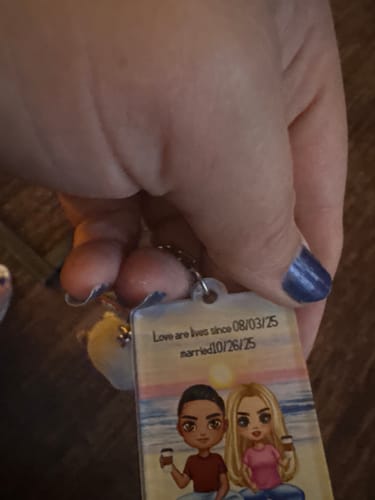 Customer's Doll Couple Personalized Acrylic Keychain held in hand, showing illustrated couple on a beach background.