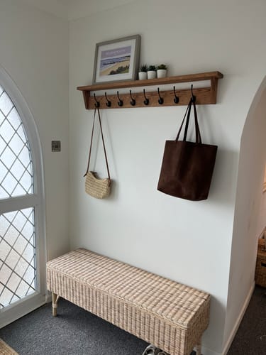 Customer's Solid Oak Walnut Coat Rack with Shelf mounted on a white wall in a hallway with bags hanging from hooks.