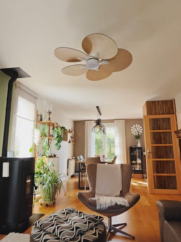 Client's Lotus fan au plafond, ventilateur en bois clair avec des pales en forme de pétales dans un salon chaleureux.