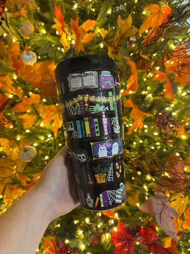 Customer's To-Go Buddy tumbler with colorful Halloween-themed book and potion illustrations against a festive tree