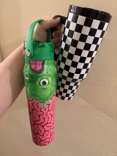Reviewer's hand holding two Frost Buddy cups, one with green brain pattern and one with a black and white checker pattern.