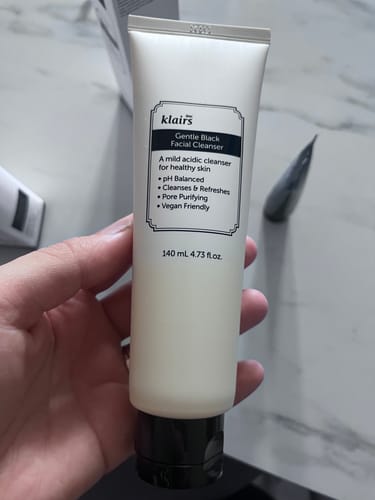 Reviewer's hand holding the white and black Gentle Black Facial Cleanser tube.