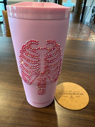 Customer's pink To-Go Buddy tumbler with a decorative sparkling skeleton rib cage design on a wooden table.