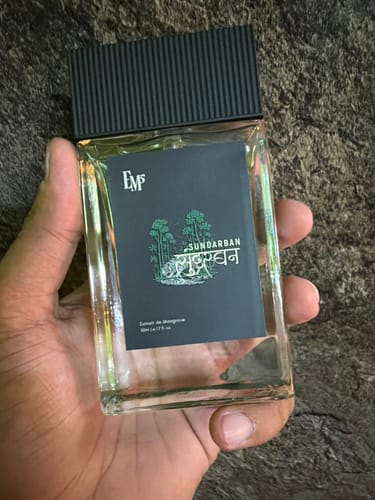 Customer's hand holding a transparent 50ml bottle of Sundarban Perfume Spray featuring a black cap and graphic label.