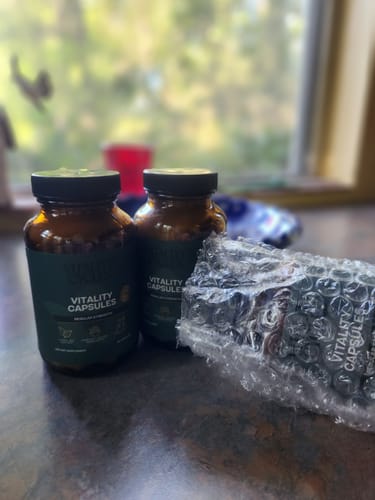 Customer's two amber glass bottles of Regular Strength Vitality Capsules, one partially wrapped in bubble wrap.