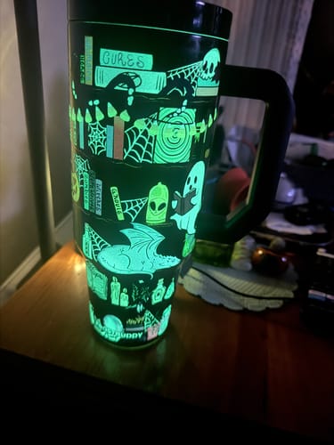 Reviewer's glowing Thicc Buddy mug in the dark, featuring spooky book and ghost illustrations.