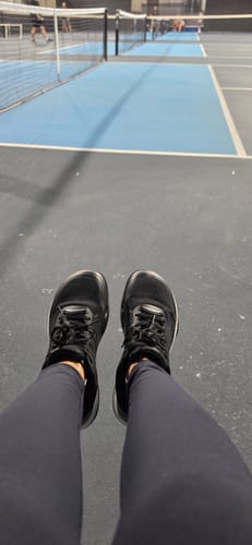 Reviewer's black CUURT Muuv court shoes being worn on a blue pickleball court.