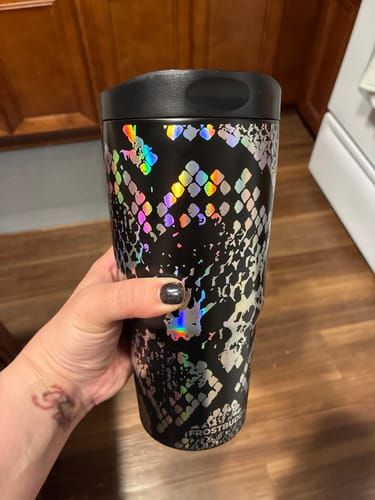 Customer's hand holding the black To-Go Buddy tumbler featuring a metallic, iridescent snake-skin pattern.