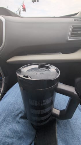 Customer's black Thicc Buddy 40oz tumbler with a closed lid, resting on their lap inside a vehicle.