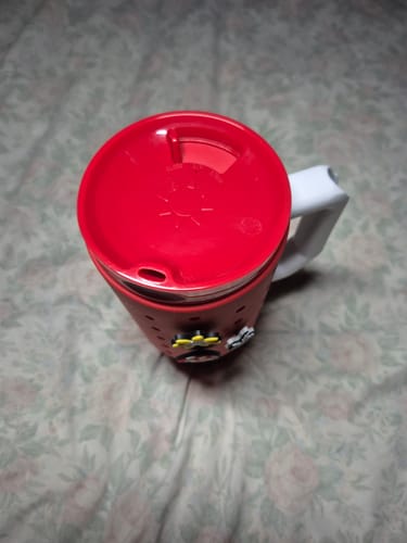 Customer's bright red ONE Lid attached to a Thicc Buddy tumbler with decorative charms on a textured fabric surface.