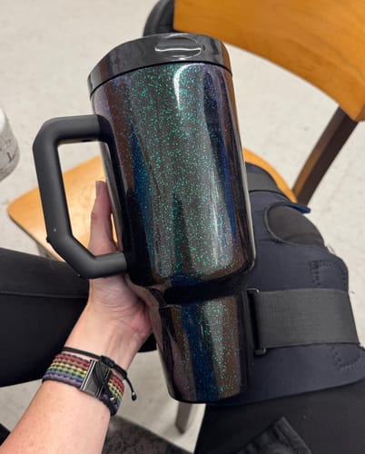 Customer's dark mermaid-colored Thicc Buddy mug with glittery finish being held in a person's hand.