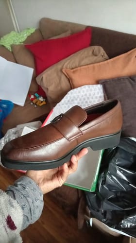 Customer's Mazerata Ilario faux wax shoe held in hand, showing its brown color and polished, slip-on design.