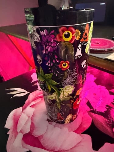 Customer's Toxic Bloom To-Go Buddy cup featuring colorful floral and spooky pattern, resting on a pink floral surface.
