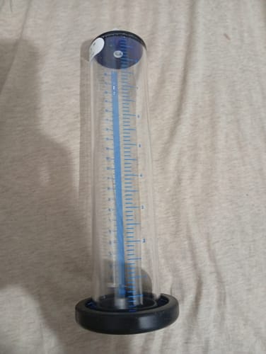 Reviewer's clear pump cylinder replacement with blue measurement markings and a black base, standing on a fabric surface.