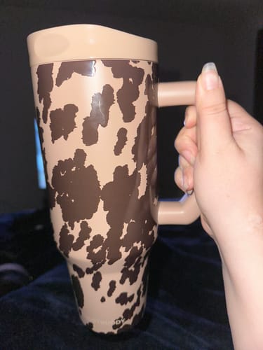 Customer's Thicc Buddy mug in cocoa cow print, held by a hand.
