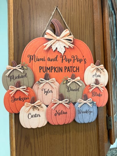 Customer's personalized Pumpkin Patch door hanger displayed on a wooden cabinet, featuring names of grandchildren.