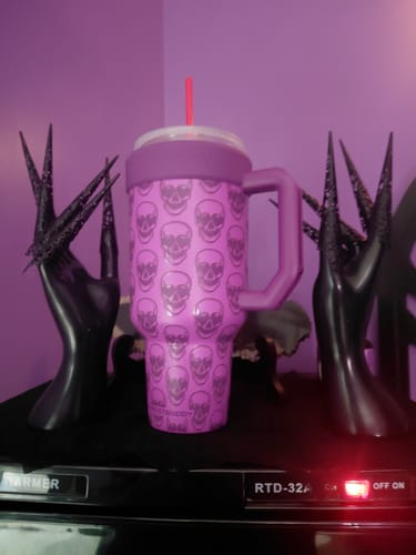 Customer's purple Thicc Buddy mug with skull print displayed between two black decorative hand sculptures.
